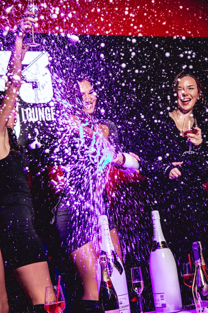 Frauen die Feiern und Sekt aus einer Flasche spritzen