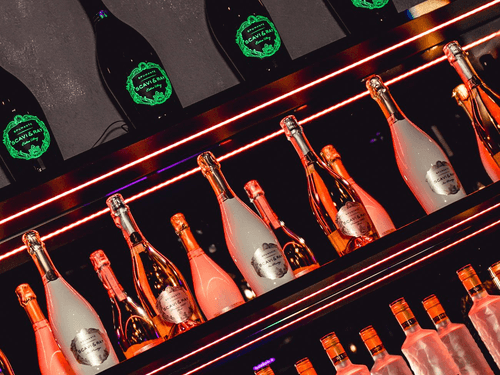 Mehrere Getränkeflaschen auf Regalen vor einer Spiegelwand